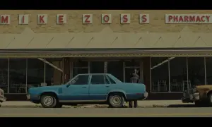 Niebieski samochód przed apteką "MIKE ZOSS PHARMACY". Obraz w stylu **false color**, z lekko zmienionymi barwami, tworzy nostalgiczny klimat.