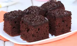 Quattro fette di torta al cioccolato morbida e umida, ricoperte di codette di cioccolato, su un piatto bianco.