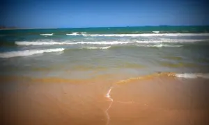 Olas rompiendo en la arena dorada, un día soleado perfecto para visitar la playa más cercana a Toledo.