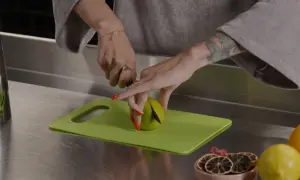 Ręce z czerwoną hybrydą kroją limonkę na zielonej desce. Obok leżą cytryny i suszone plasterki cytrusów, idealne do kordiałów.