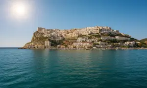 La spiaggia La Cala di Peschici, con le sue case bianche aggrappate alla roccia, si specchia nel mare blu sotto un sole splendente.