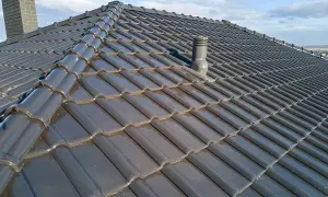 Szary dach z dachówki ceramicznej, z widocznym kominkiem wentylacyjnym i kominem. Rozmieszczenie kominków wentylacyjnych na dachu zapewnia prawidłową cyrkulację powietrza.