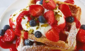 Goldbraune Waffeln mit Sahne, Erdbeeren, Blaubeeren und Erdbeersauce, bestreut mit Pistazien. Ein süßer Genuss!
