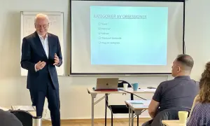 Föreläsare presenterar "Kategorier av obsessioner" som steg 1 i en utbildning. Publiken lyssnar uppmärksamt.