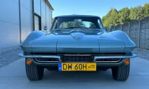 Klasyczny zielony Corvette C2 z lat 60. stoi przed nowoczesnym budynkiem.