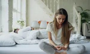 Een vrouw zit op bed, nadenkend na een ruzie. Haar partner slaapt ernaast. Ze is een hsp en voelt de spanning nog.