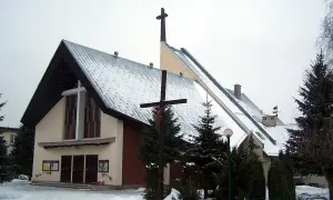 Kościół w Robakowie zimą, pokryty śniegiem, z krzyżem przed fasadą.