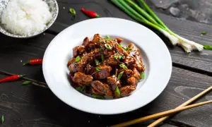 Pyszny kurczak po wietnamsku w sosie, posypany sezamem i szczypiorkiem, obok miseczka ryżu i papryczki chili.