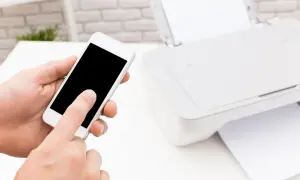 Dłoń trzyma smartfon, obok drukarka HP. Prosty sposób, jak drukować z telefonu na drukarce HP przez WiFi.