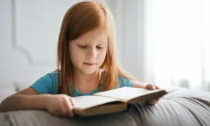 Niña pelirroja concentrada leyendo un libro. Su velocidad lectora por edades es notable para su corta edad.