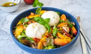 Pfirsich-Burrata-Salat mit Nüssen und Basilikum in blauer Schüssel.