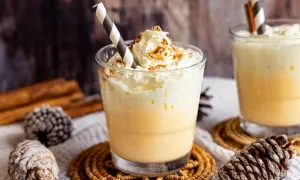 Zwei Gläser Bombardino mit Sahne und Zimt, dekoriert mit Tannenzapfen und Zimtstangen.