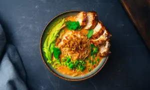 Aksamitny, kremowy tan tan ramen z kawałkami grillowanego kurczaka, chrupiącą cebulką i świeżą kolendrą.