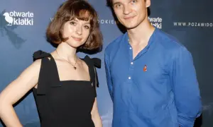 Kasia Sienkiewicz w czarnej sukience i mężczyzna w niebieskiej koszuli z liskiem na piersi pozują na tle niebieskiej ścianki z logo "otwarte klatki".