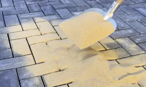Schaufel mit Sand zum Pflastersteine verfugen. Sand rieselt auf dunkle Steine, um Fugen zu füllen.
