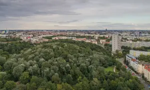 Luftaufnahme des Volksparks Friedrichshain mit dichtem Baumbestand und Berliner Skyline im Hintergrund.