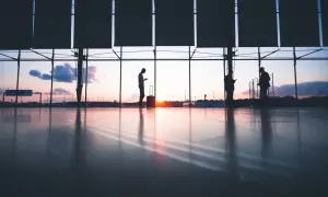 Sylwetki ludzi z bagażami czekają na lotnisku o zachodzie słońca. Czy to przez overbooking Ryanair?