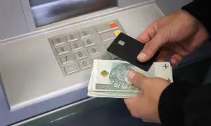 Ręce trzymające banknoty i kartę zbliżają się do wpłatomatu. Pieniądze na koncie czekają na wpłatę.