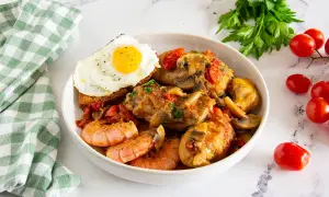Un saporito pollo alla Marengo con gamberi, funghi e pomodorini, servito con pane tostato e uovo fritto.