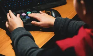 Dłonie gracza na joysticku i klawiaturze, obok myszka komputerowa.