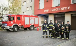 Strażacy OSP Czechowice z wozem strażackim i dziećmi w strojach strażackich.