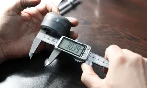 Dłoń trzymająca suwmiarkę cyfrową mierzącą metalowy element.