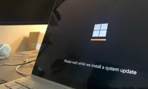 Ekran laptopa z logo Windows i komunikatem "Please wait while we install a system update". To ważny etap, jak aktualizować sterowniki, by system działał sprawnie.