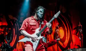 Muzyk Slipknot w czerwonym kombinezonie i masce gra na białej gitarze. Zapowiedź nowego albumu Slipknot.