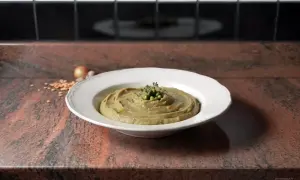 Une assiette de purée de pois cassés, garnie de petits pois et d'herbes, sur un plan de travail en granit.