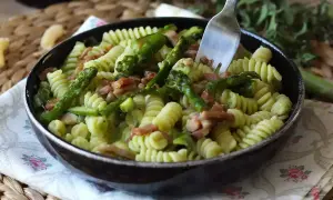 En härlig pastarätt med sparris och bacon, perfekt för ett snabbt sparris recept. En gaffel sticker upp ur den krämiga pastan.