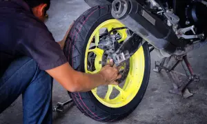 Mechanik wymieniający oponę w motocyklu z żółtą felgą.