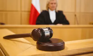 Młotek sędziowski na stole w sali sądowej, obok polska flaga. Sędzia w todze w tle. Ile apelacji jest oddalanych?