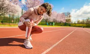 Frau mit Kniearthrose hält ihr schmerzendes Knie auf einer Laufbahn.
