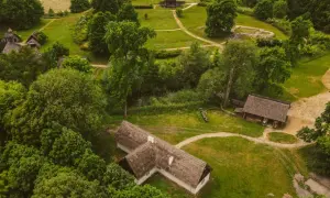 Rezerwat archeologiczny Zawodzie, z widokiem na drewniane chaty i zalesione wzgórza, ukazuje dawne osadnictwo.