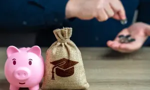 Różowa świnka-skarbonka i worek z symbolem czapki absolwenta na drewnianym stole.