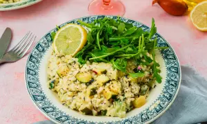 Un crémeux risotto courgette, garni de roquette fraîche et d'une tranche de citron, sur une assiette ornée.