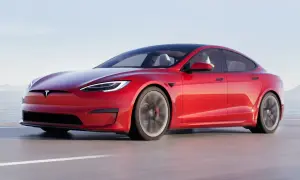 Czerwony Tesla Plaid pędzi po drodze, z widokiem na morze i góry w tle.