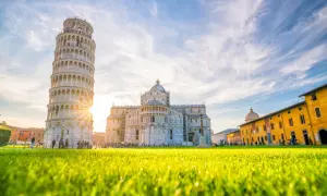 La Torre di Pisa, Italia, brilla sotto un cielo azzurro con nuvole bianche. L'erba verde brillante in primo piano cattura la luce del sole.