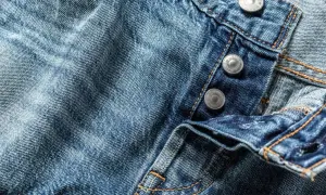 Zbliżenie na niebieski jeansowy materiał z widocznymi guzikami i przeszyciami.