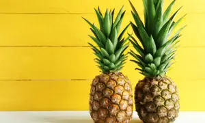 Dwa soczyste ananasy na tle żółtej deski. Poznaj ich bogactwo witamin i minerałów – ananas wartości odżywcze.