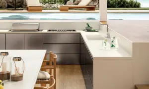 Moderna encimera para exterior con barbacoa integrada, junto a una piscina y tumbonas.