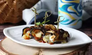Grillad aubergine rullad med ost och tomatsås, serverad på en vit tallrik. Perfekt för picknick!