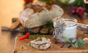 Pasztet na chlebie z ziołami, słoik pasztetu, chleb i papryczka chili na desce.