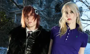 Frost Children setlist: A person with red hair and a black furry jacket stands next to a person with blonde hair in a purple polo shirt.