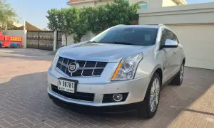 Srebrny Cadillac SRX z Dubai stoi na podjeździe przed domem. Obok widać bramę i fragment czerwonej zabawki.