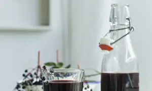 Sok z czarnego bzu przepis babci. Ciemny, zdrowy napój w szklance i butelce, ozdobiony gałązką z owocami.