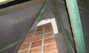 Drewniana konstrukcja dachu z widoczną stopą pod komin, obłożoną cegłą i izolacją.