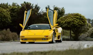 Żółty Lamborghini Diablo z otwartymi drzwiami, zaparkowany na drodze wśród zieleni.