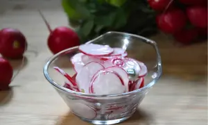 Pyszna surówka z rzodkiewki do obiadu, w szklanej miseczce, z kilkoma rzodkiewkami w tle.