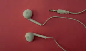 Białe słuchawki douszne czy dokanałowe z wtyczką jack na różowym tle.